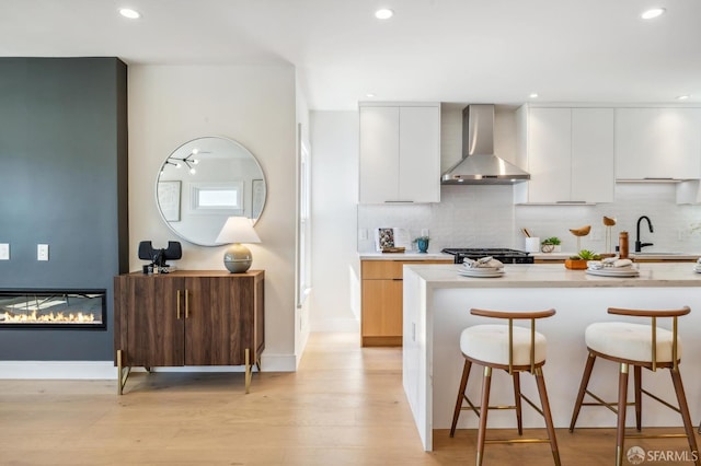 kitchen featuring white cabinetry, wall chimney range hood, tasteful backsplash, and sink