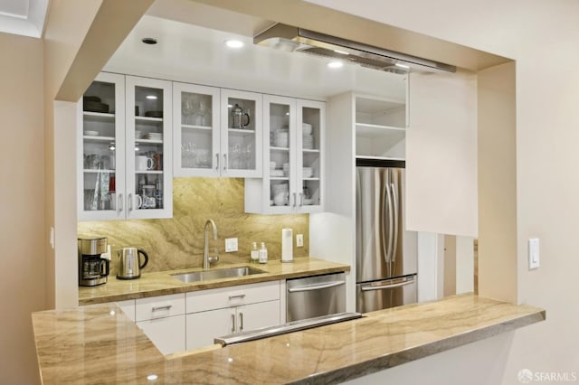 kitchen featuring white cabinets, appliances with stainless steel finishes, light stone counters, a sink, and backsplash