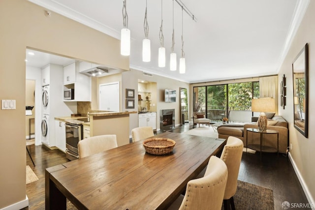 dining room featuring dark wood-style floors, stacked washer and dryer, ornamental molding, and a fireplace