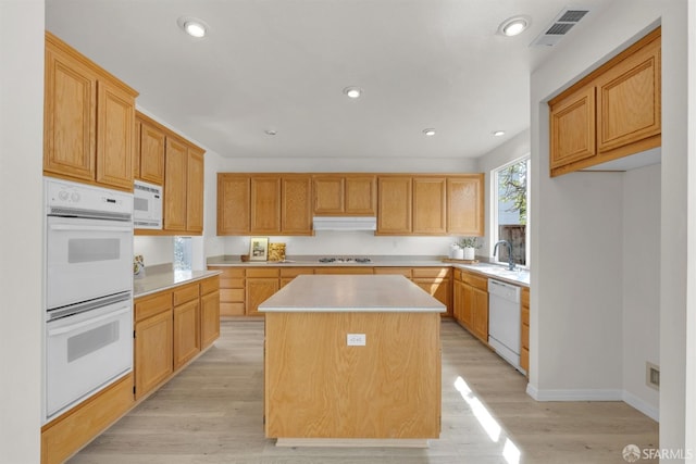 kitchen featuring light wood-style floors, visible vents, a kitchen island, light countertops, and white appliances