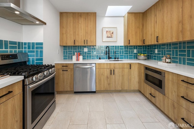 kitchen featuring sink, a skylight, appliances with stainless steel finishes, wall chimney range hood, and backsplash