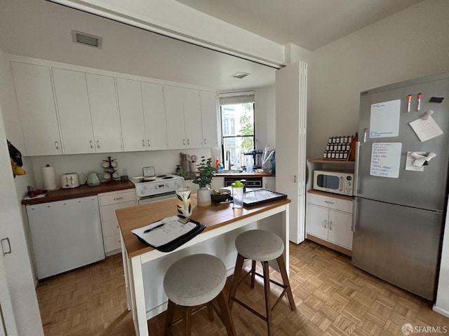 kitchen with visible vents, white cabinetry, white appliances, and wooden counters