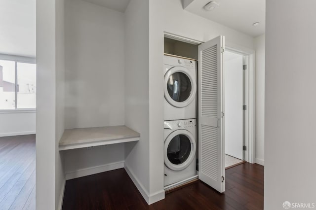 clothes washing area with dark wood-style flooring, laundry area, baseboards, and stacked washing maching and dryer