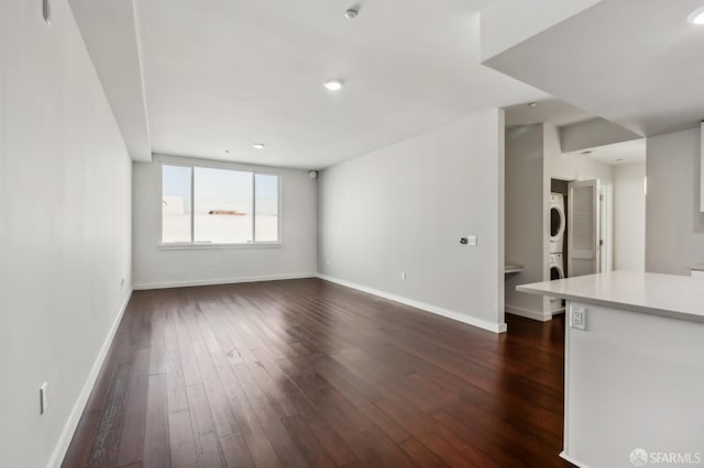 unfurnished living room featuring dark wood-style floors, stacked washing maching and dryer, and baseboards