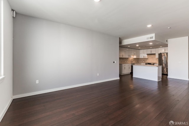 unfurnished living room with baseboards, visible vents, dark wood-type flooring, a sink, and recessed lighting