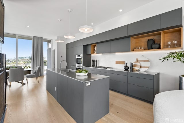 kitchen featuring a center island with sink, sink, hanging light fixtures, light hardwood / wood-style flooring, and appliances with stainless steel finishes