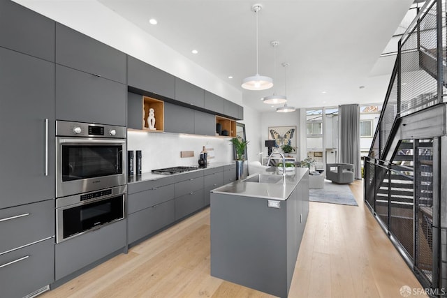 kitchen featuring gray cabinetry, a kitchen island with sink, sink, pendant lighting, and light hardwood / wood-style flooring