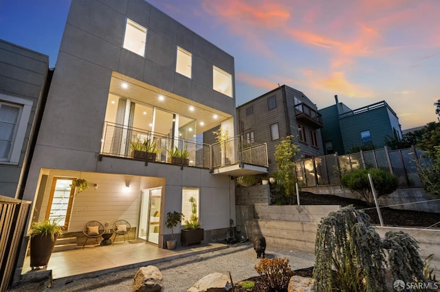 back house at dusk featuring a patio and a balcony