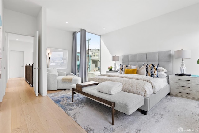 bedroom with light hardwood / wood-style flooring, a wall of windows, and lofted ceiling