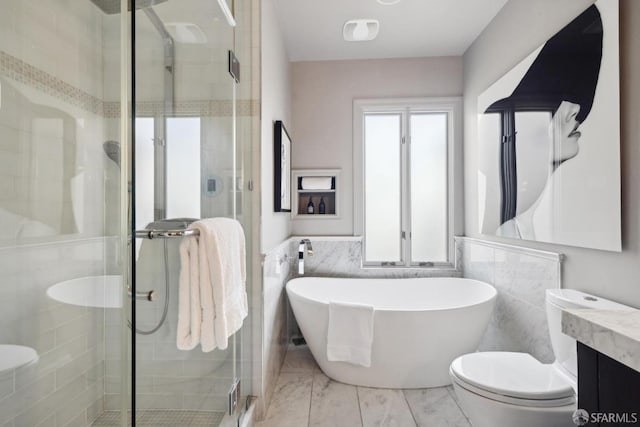 bathroom with a stall shower, wainscoting, toilet, a freestanding tub, and tile walls