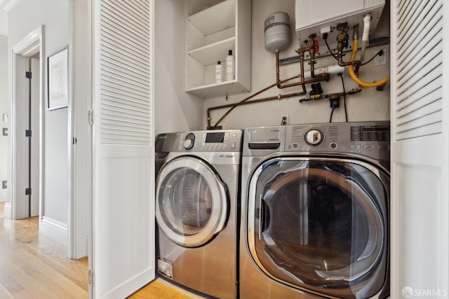 clothes washing area featuring light wood-type flooring, laundry area, and washer and clothes dryer