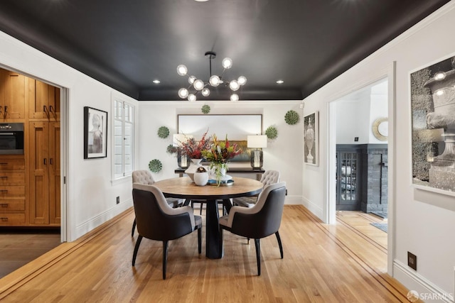 dining space with light wood-type flooring, baseboards, and an inviting chandelier