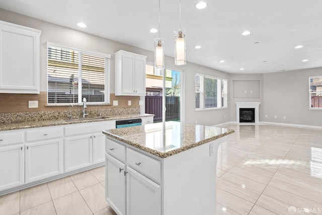 kitchen with pendant lighting, sink, white cabinetry, a center island, and light stone countertops