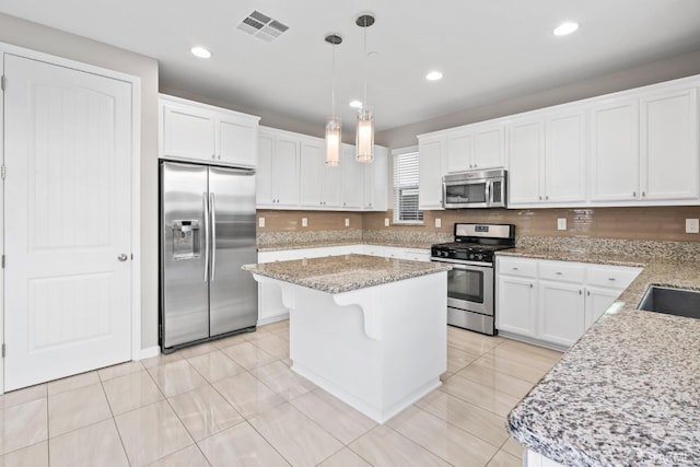 kitchen with white cabinetry, stainless steel appliances, light stone counters, a kitchen island, and decorative light fixtures