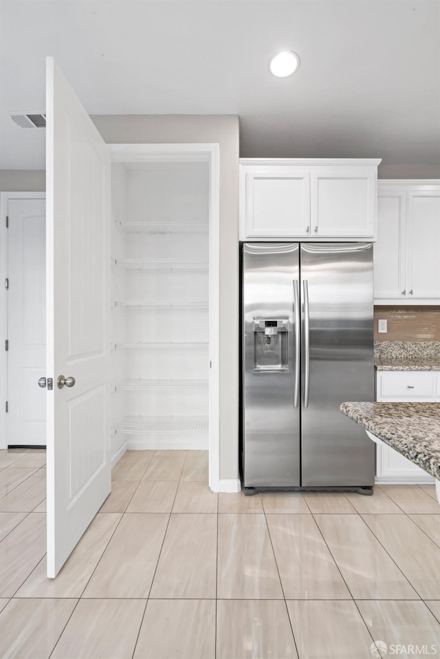 kitchen with stainless steel refrigerator with ice dispenser, light stone counters, light tile patterned floors, white cabinets, and backsplash