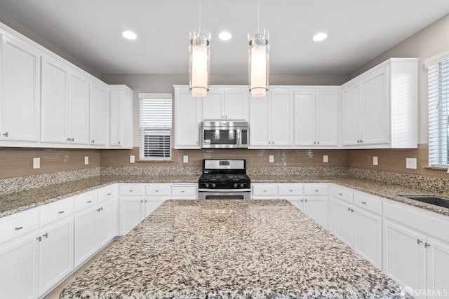 kitchen featuring appliances with stainless steel finishes, white cabinetry, hanging light fixtures, light stone counters, and a wealth of natural light