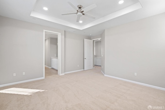 unfurnished bedroom featuring a raised ceiling, ensuite bathroom, light carpet, and ceiling fan