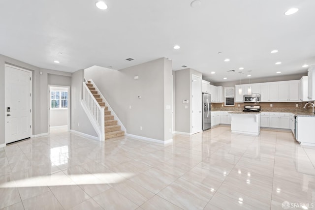 kitchen featuring sink, white cabinetry, a center island, appliances with stainless steel finishes, and backsplash