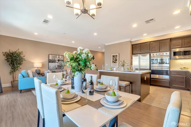 dining area with light hardwood / wood-style floors, crown molding, and an inviting chandelier