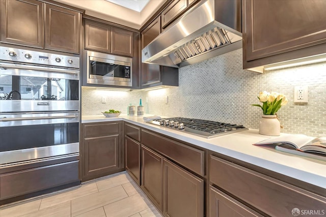 kitchen with exhaust hood, dark brown cabinets, backsplash, and appliances with stainless steel finishes