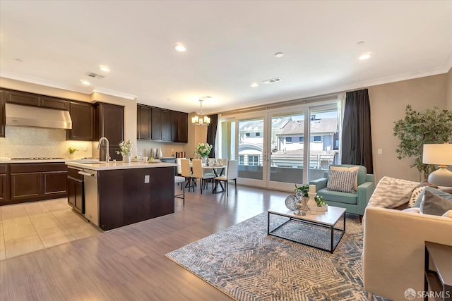 kitchen featuring extractor fan, decorative backsplash, dark brown cabinets, pendant lighting, and an island with sink