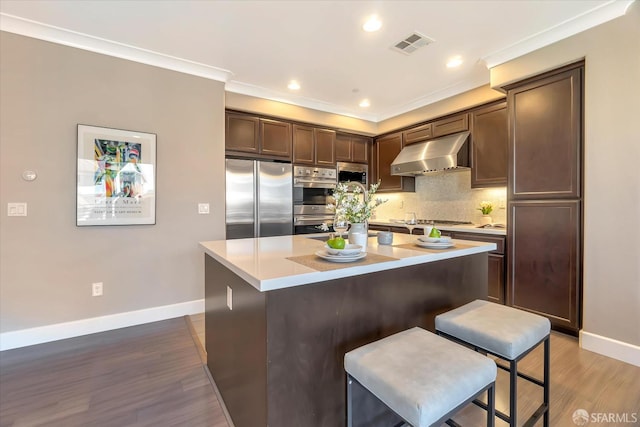 kitchen with a center island, exhaust hood, a kitchen bar, appliances with stainless steel finishes, and backsplash