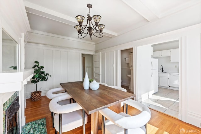 dining area with beamed ceiling, an inviting chandelier, sink, and light wood-type flooring