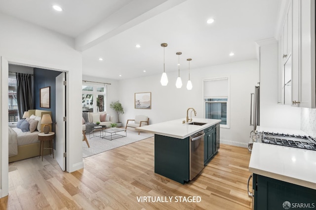 kitchen with hanging light fixtures, appliances with stainless steel finishes, sink, white cabinets, and a center island with sink