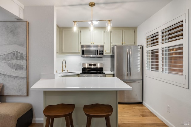 kitchen featuring sink, a breakfast bar area, hanging light fixtures, stainless steel appliances, and kitchen peninsula