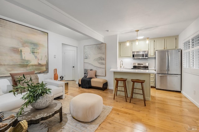 kitchen with a breakfast bar, sink, hanging light fixtures, light hardwood / wood-style floors, and stainless steel appliances