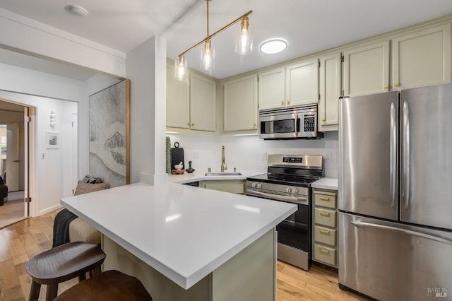 kitchen featuring appliances with stainless steel finishes, sink, a kitchen breakfast bar, light hardwood / wood-style floors, and kitchen peninsula