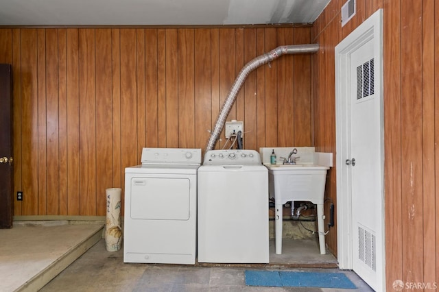 laundry area featuring wood walls, washing machine and dryer, and sink