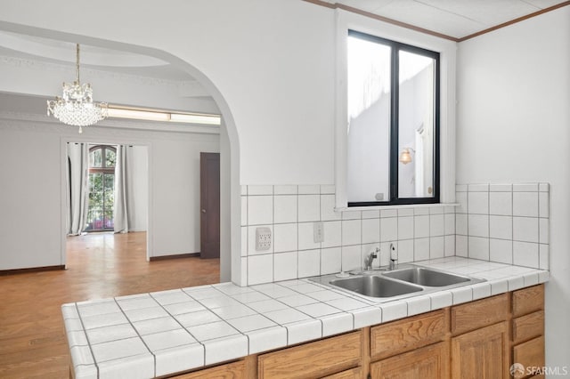 kitchen featuring tile countertops, an inviting chandelier, sink, hanging light fixtures, and ornamental molding