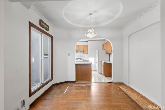 unfurnished dining area featuring a notable chandelier, light hardwood / wood-style flooring, and a tray ceiling