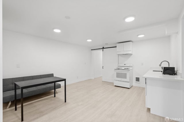 kitchen with electric stove, sink, a barn door, light hardwood / wood-style floors, and white cabinetry