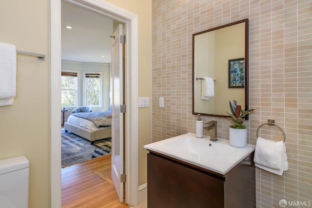 ensuite bathroom featuring tasteful backsplash, connected bathroom, toilet, wood finished floors, and vanity