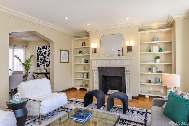 living room with built in shelves, arched walkways, crown molding, a fireplace, and baseboards