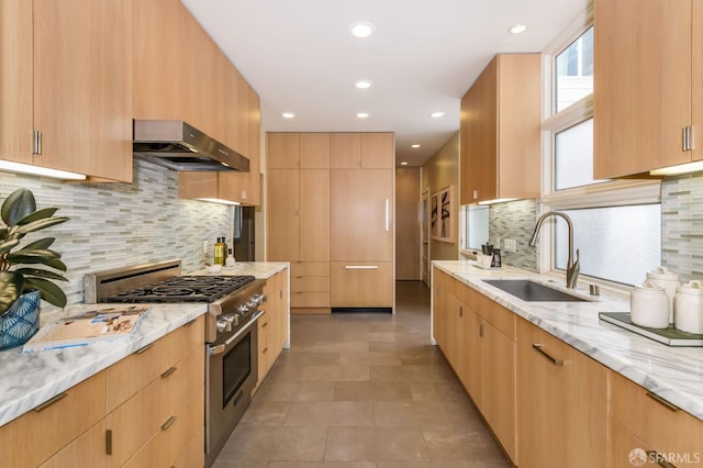 kitchen featuring light stone countertops, stainless steel stove, a sink, modern cabinets, and under cabinet range hood