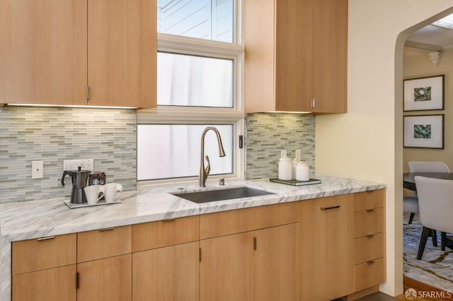 kitchen with light stone counters, arched walkways, a sink, and tasteful backsplash