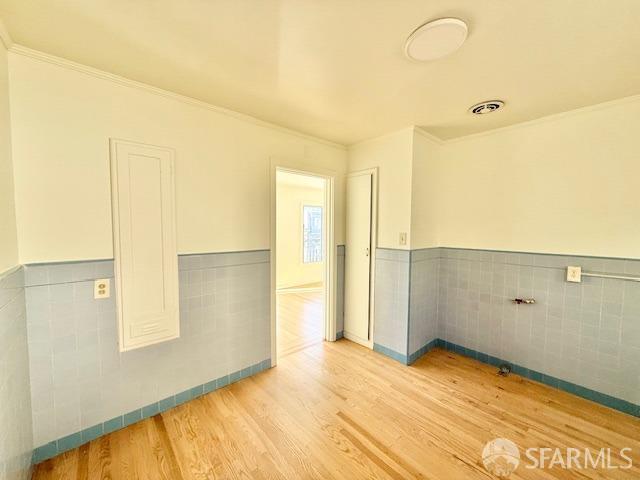 empty room featuring crown molding, light hardwood / wood-style floors, and tile walls