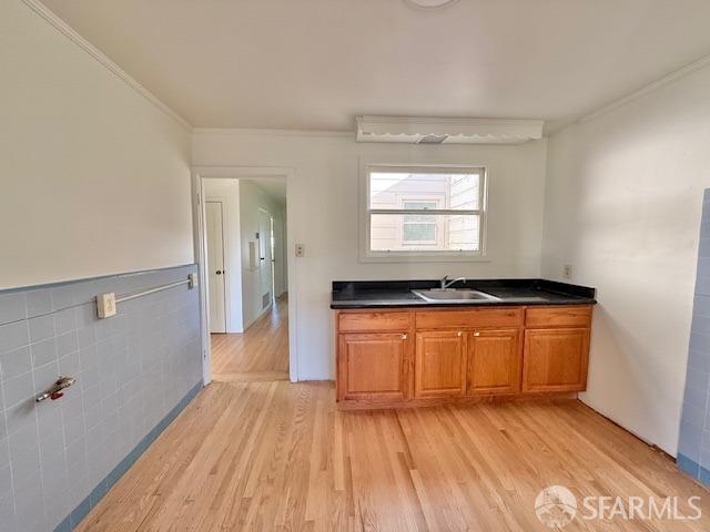 kitchen with crown molding, sink, tile walls, and light hardwood / wood-style flooring