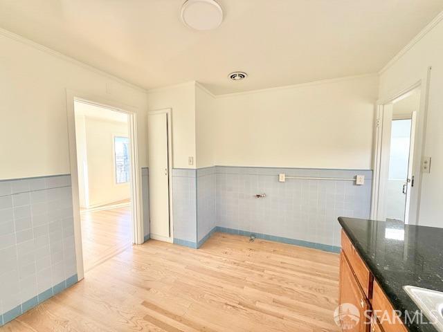 kitchen featuring dark stone counters, light hardwood / wood-style floors, tile walls, and ornamental molding