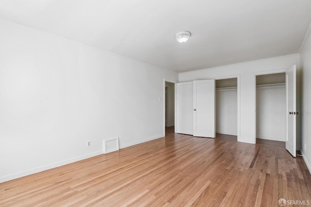 unfurnished bedroom featuring light hardwood / wood-style flooring and multiple closets