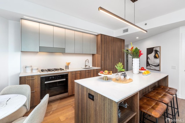 kitchen with white gas cooktop, sink, light hardwood / wood-style flooring, oven, and decorative light fixtures