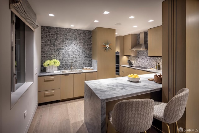 kitchen with backsplash, wall chimney range hood, light hardwood / wood-style flooring, a breakfast bar, and sink