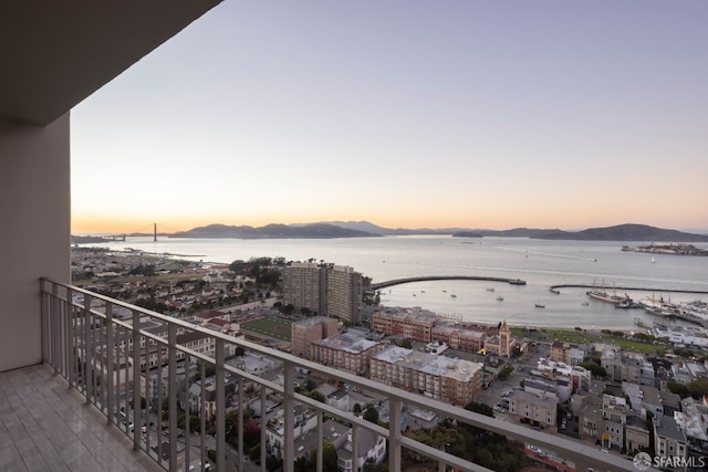 balcony at dusk featuring a water and mountain view