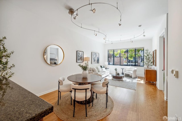 dining area featuring light wood-type flooring, rail lighting, and baseboards