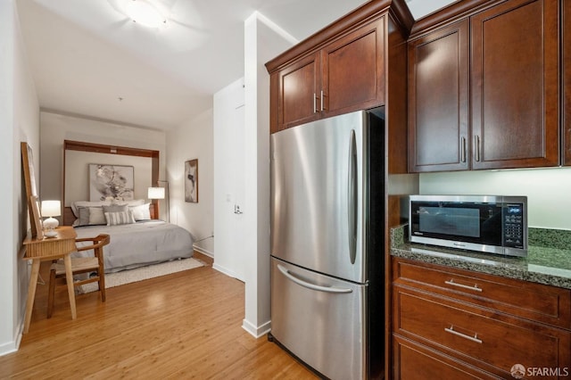 kitchen featuring baseboards, appliances with stainless steel finishes, open floor plan, dark stone countertops, and light wood-style floors