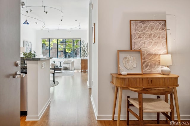 hallway with baseboards, track lighting, and wood finished floors