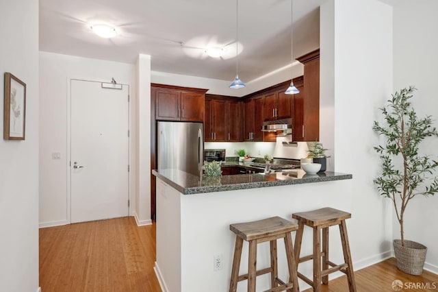 kitchen with decorative light fixtures, a breakfast bar area, freestanding refrigerator, light wood-type flooring, and a peninsula